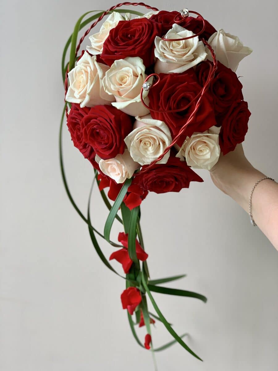 Bouquet de mariée rond rouge et crème avec une retombée en feuillage et pétales de roses stabilisées